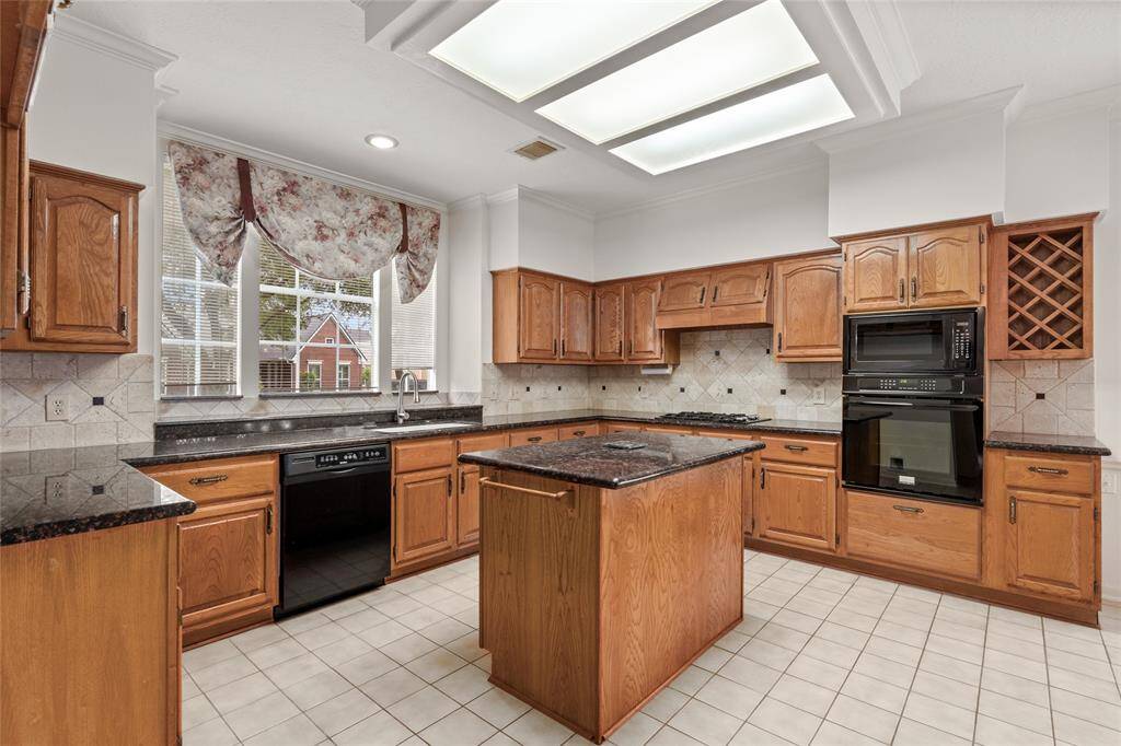 From this angle, the kitchen showcases its generous layout with a clear view of the expansive counter space and cabinetry. The warm wood-paneled cabinets continue to provide both style and function, while the wide window offers a glimpse of natural light, brightening the entire room. The open space around the center counter creates a welcoming atmosphere, perfect for prepping meals or casual conversation.