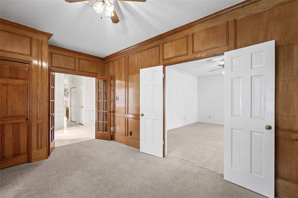 The richly paneled home office impresses with a fireplace, French doors, and ceiling fan, offering warmth and privacy. A set of double doors leads to an adjoining bonus room—perfect for a second office, hobby space, or additional living area—enhancing the home's flexibility and flow.