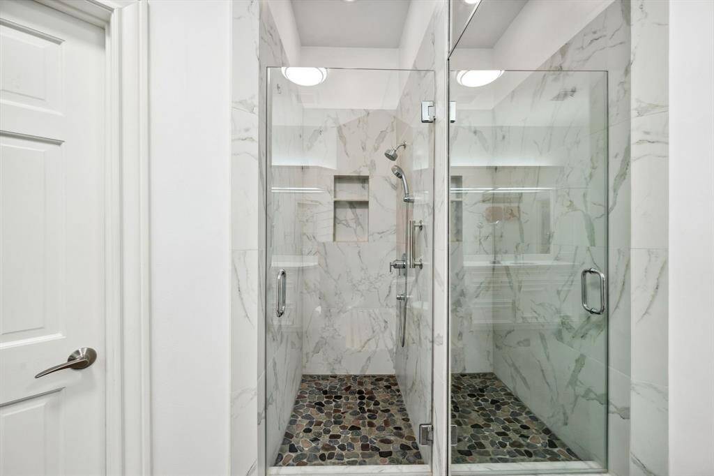 This home features elegant dual primary suite baths, with one highlighting a stunning soaking tub framed by beautiful arched windows, creating a spa-like experience. Luxury tiles run throughout the baths and into the spacious walk-in closets, adding a touch of sophistication and seamless flow.