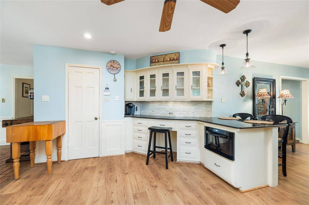 This spacious kitchen boasts a convenient study nook, perfect for meal planning or a quiet workspace. A beautiful stone backsplash complements the sleek black granite countertops, which stand out against the crisp white cabinetry, blending style with functionality.