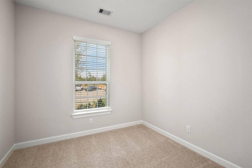The secondary bedroom has a large window and comfortable carpet flooring.