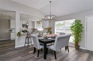This photo showcases a bright dining area with modern decor. It opens to a sleek kitchen with stainless steel appliances and bar seating. Large windows and walls enhance the spacious feel.