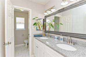 Bright and modern bathroom featuring a double vanity with granite countertops, large mirror, and ample lighting. There's a separate toilet area and a touch of greenery for a fresh feel.