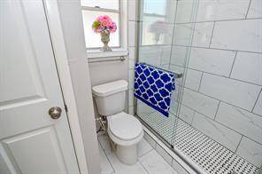 This is a modern bathroom featuring a glass-enclosed shower with white tile, a toilet, and a window with natural light.