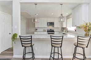 Modern kitchen with a bright, open layout. Features a large island with granite countertops and pendant lighting. White cabinetry and stainless-steel appliances add a sleek touch.
