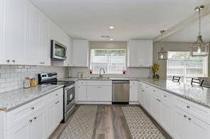 Bright, modern kitchen with white cabinets, stainless steel appliances, and granite countertops. Features a large window for natural light, subway tile backsplash, and stylish pendant lighting. Open layout with ample counter space.