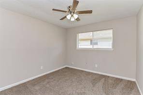 This bedroom features neutral walls, a carpeted floor, a ceiling fan with lights, and a window for natural light.