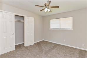 This is a bright, neutral-toned bedroom featuring carpeted flooring, a ceiling fan with lights, a window for natural light, and a closet with sliding doors.
