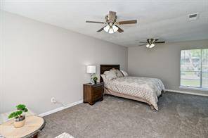 Spacious bedroom with neutral walls and carpet, featuring two ceiling fans and large windows providing natural light. The room includes a setting area.
