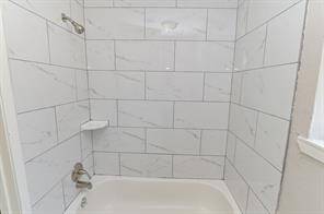 This bathroom features a clean, modern tub with white tiles and subtle gray veining. It includes a small corner shelf for convenience.