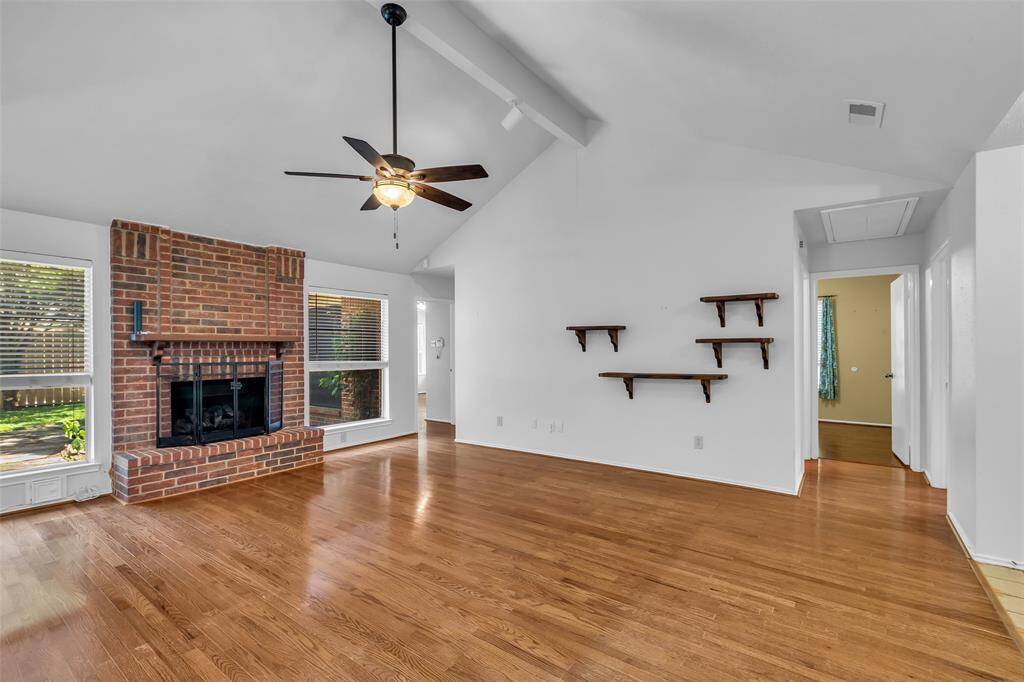 Spacious Family Room has a high cathedral ceiling, ceiling fan with lighting and spot lighting. This view shows access to the primary bedroom on the left and the secondary living area on the right.
