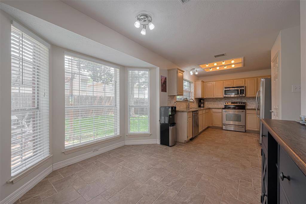Bright and inviting kitchen with large windows offering garden views. Features modern stainless steel appliances, ample cabinetry, and elegant tile flooring, perfect for culinary enthusiasts.