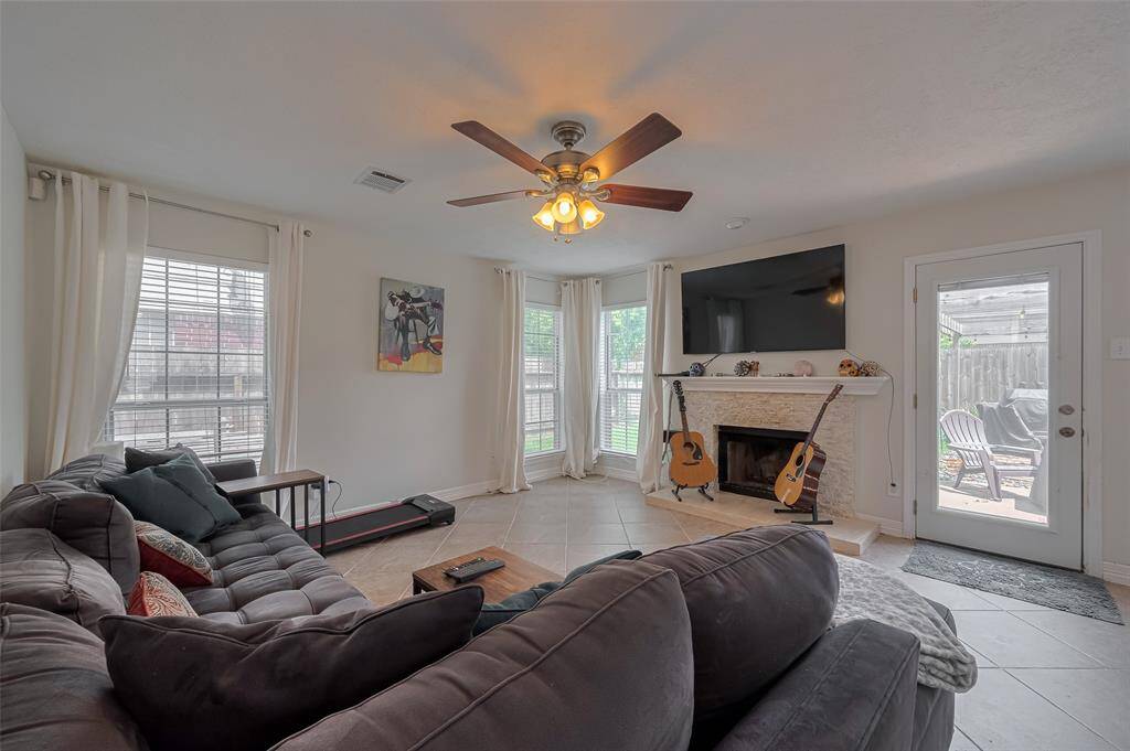 Lovely and inviting Family Room featuring a modern ceiling fan and a charming fireplace. Abundant natural light streams through large windows, enhancing the spacious feel. The room seamlessly connects to the outdoor patio, perfect for entertaining or relaxing.