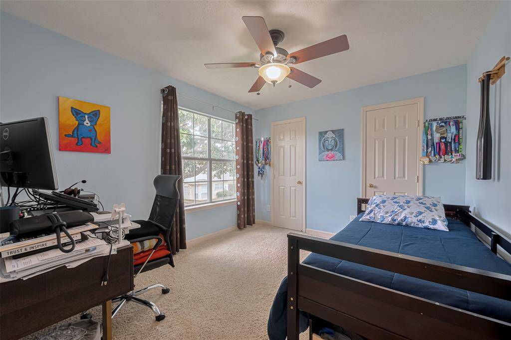 Bright and welcoming bedroom featuring a large window for natural light, soft carpeting, and a ceiling fan for comfort. Ideal for relaxation or productivity, with ample space for a desk and personal touches.