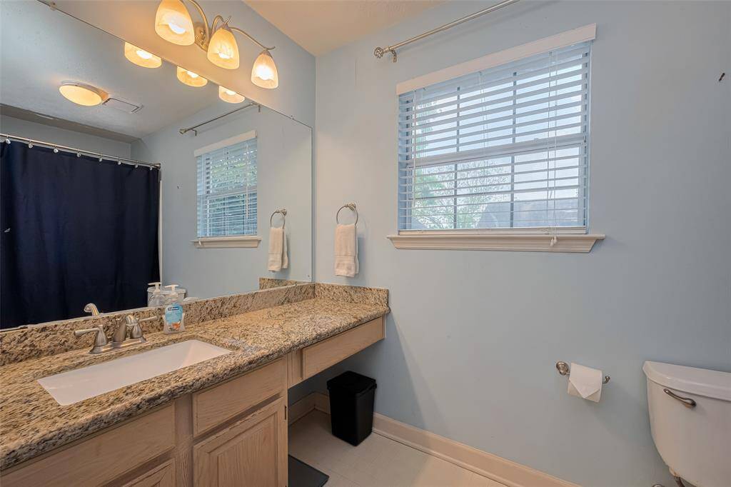 Elegant secondary bathroom featuring granite countertop, ample storage, and modern lighting.