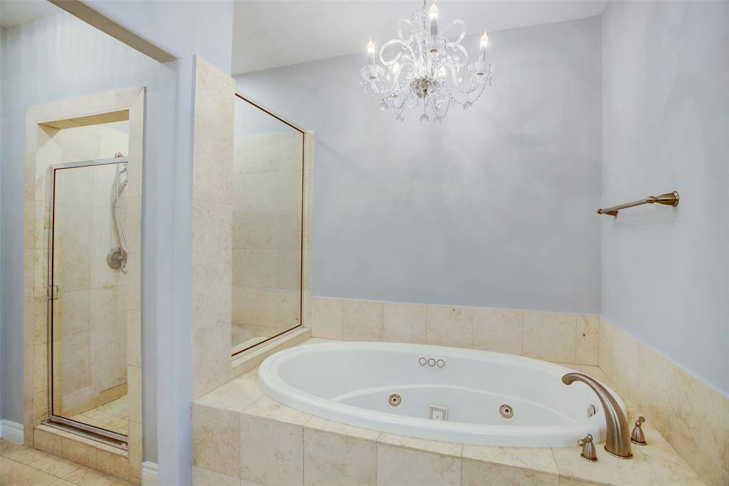 Primary bath whirlpool tub with chandelier plus separate large walk in shower with bench.