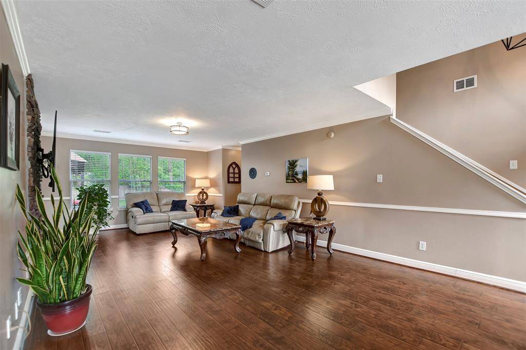 This spacious living room features hardwood floors, a neutral color palette, and abundant natural light from large windows.