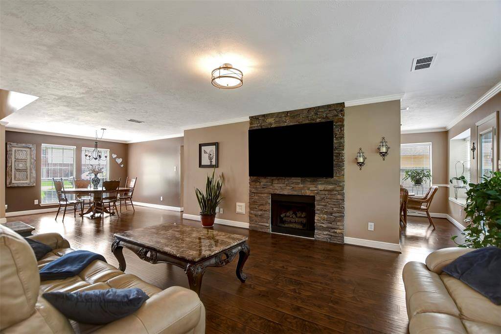 This spacious living area features hardwood flooring, a cozy stone fireplace, and a mounted TV.