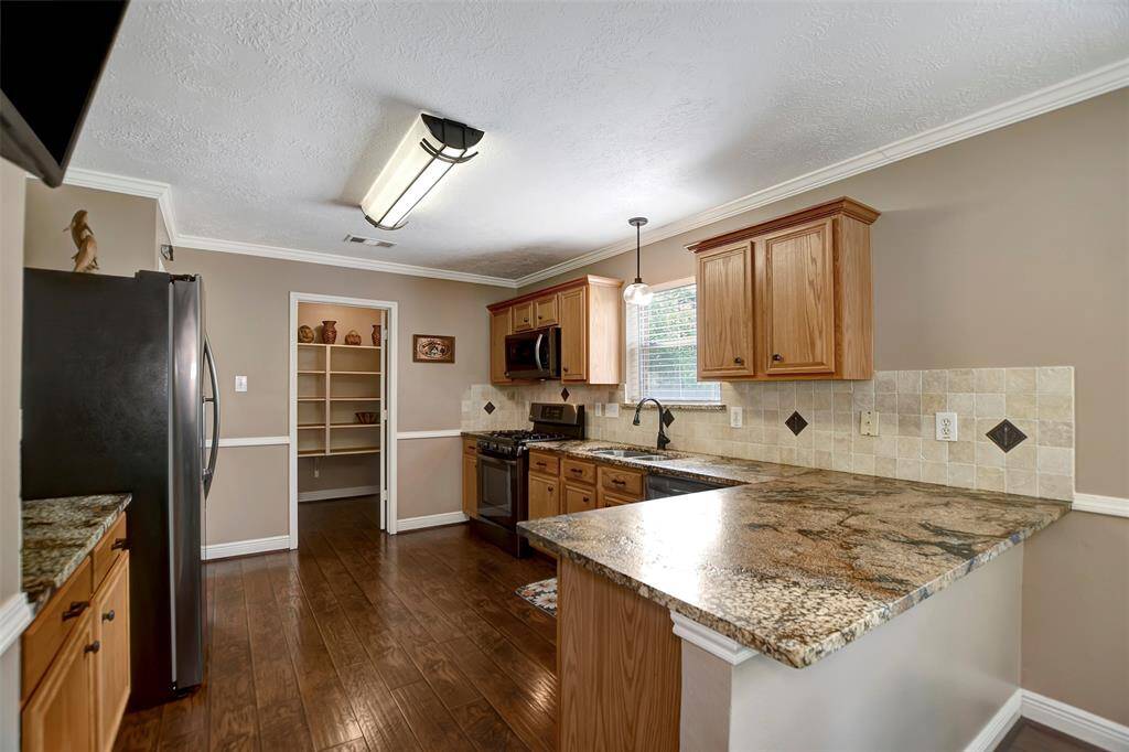 This kitchen features granite countertops, wooden cabinets, tile backsplash and stainless steel appliances.