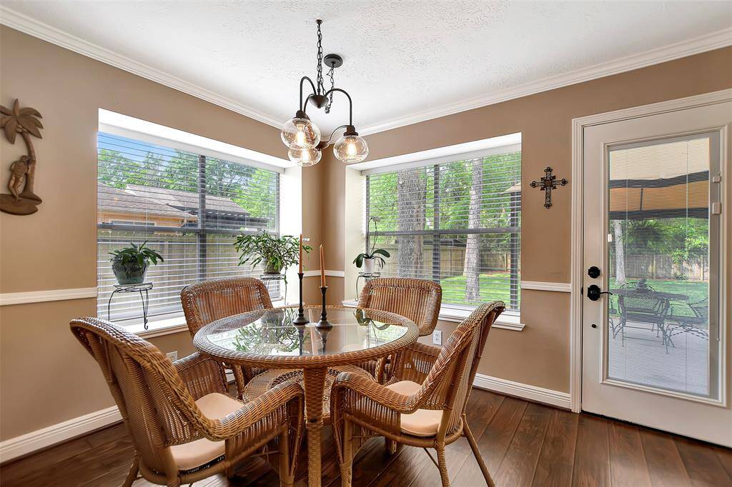 Bright breakfast area with large windows, offering views of a backyard. Features warm-toned walls, and a stylish light fixture. Ideal for enjoying meals.