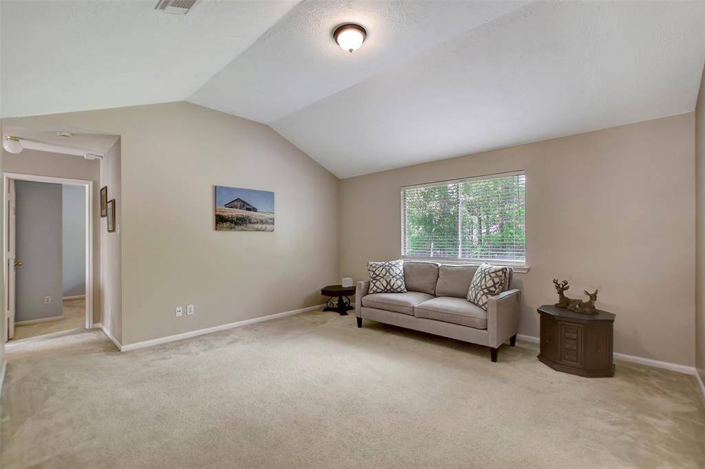 Upstairs game room splits the primary suite from the 3 secondary bedrooms.  The space has neutral walls and carpet, a vaulted ceiling, and a large window allowing natural light to fill the area.