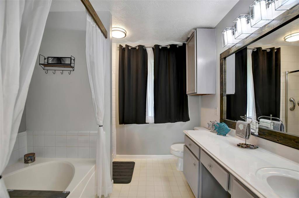 The primary bathroom has a large vanity and mirror, modern lighting, and a separate shower plus a soaking tub with curtain.