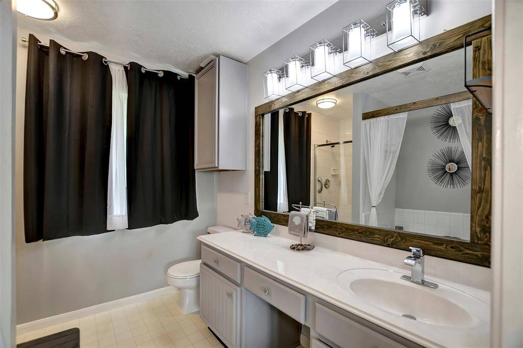 Modern bathroom featuring a large mirror with stylish lighting, and a shower with glass doors.