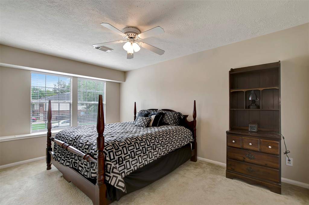 This secondary bedroom features a large window for natural light, a ceiling fan, and neutral walls.