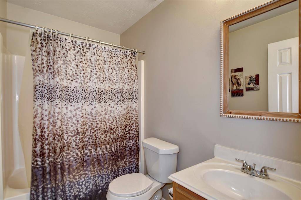This bathroom features a neutral color palette with a shower-tub combo, a newer toilet, a vanity with a sink, and a decorative mirror.
