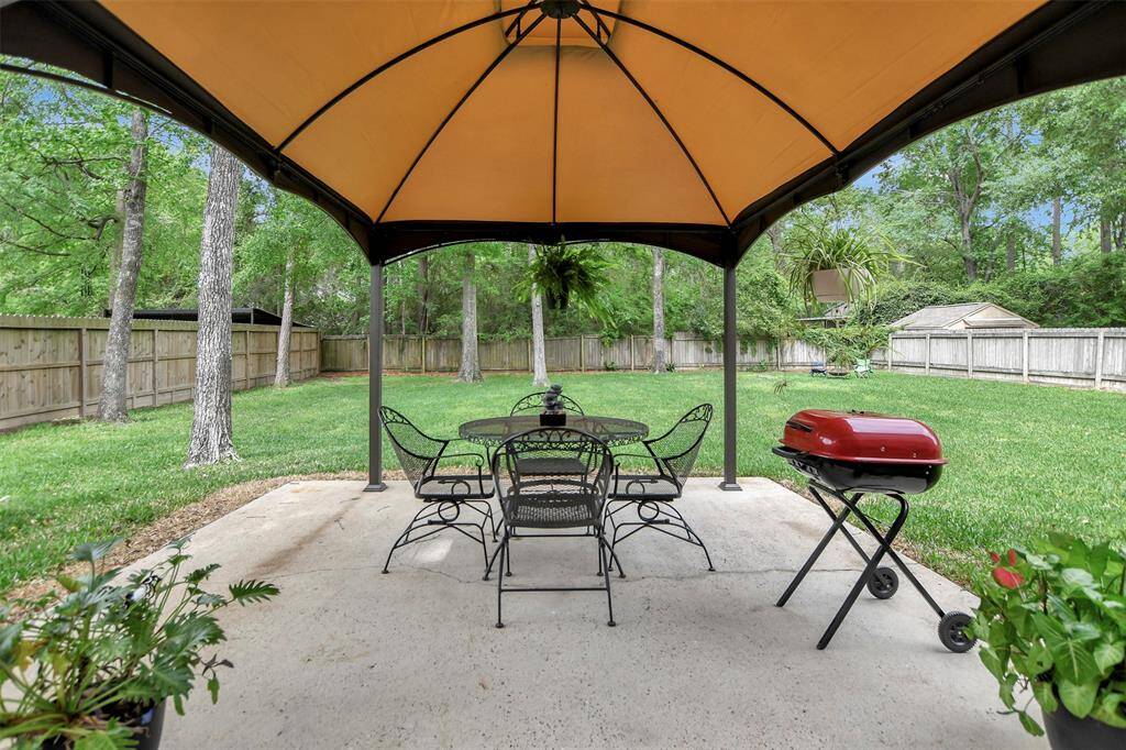 The backyard patio with a canopy is surrounded by lush greenery and a fenced yard, perfect for entertaining and relaxation.