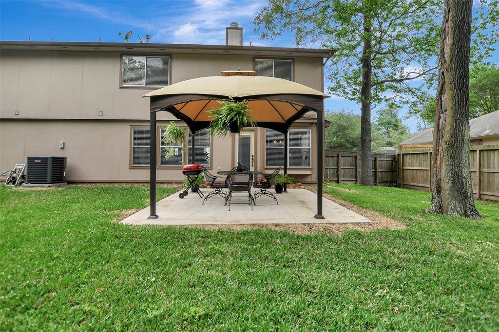 This backyard features a spacious lawn with a cozy gazebo on a concrete patio (approx. 15x13), ideal for outdoor dining and relaxation. The area is enclosed by a wooden fence, providing privacy, and mature trees offer shade and a natural backdrop.