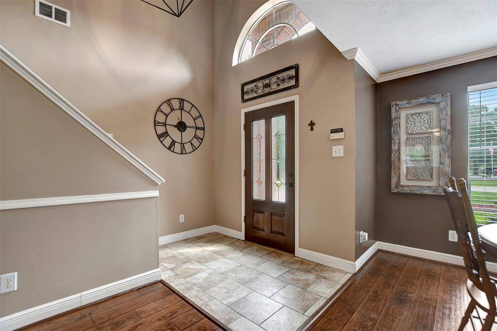 Bright entryway with a large window above the door. Features tiled flooring transitioning to wood with access to a dining area with ample natural light.