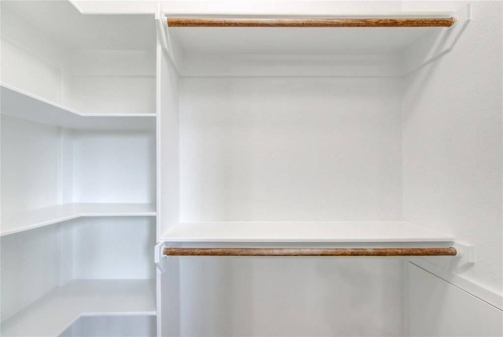 This a photo is of spacious walk-in closet in bedroom #2 with white custom built-in shelves and wooden hanging rods, offering ample storage for clothing and accessories.