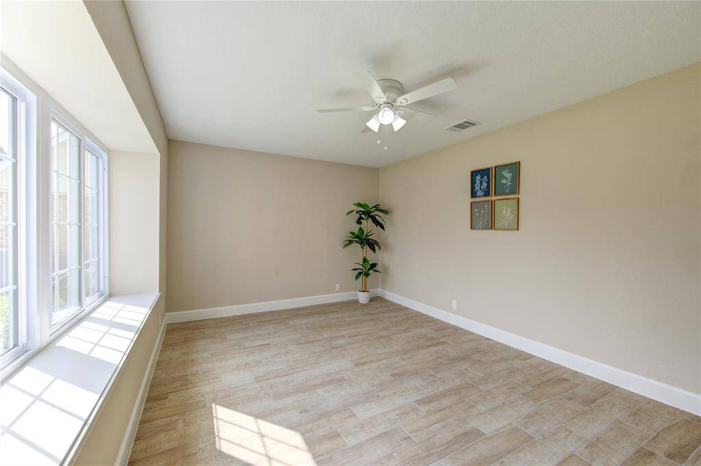 This flex space is to the left of the entryway provides an excellent spot for an office, craft room, or anything that fits your style. It features large new windows that allow ample natural light, a ceiling fan, light wood-like tile flooring, and neutral walls, creating an open and airy atmosphere.
