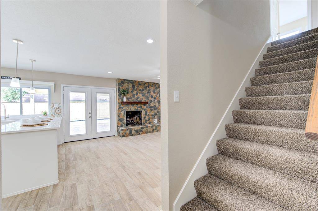 This photo showcases a bright living area featuring a stone fireplace and large glass doors leading outside. The open-plan kitchen area is visible with modern pendant lighting.