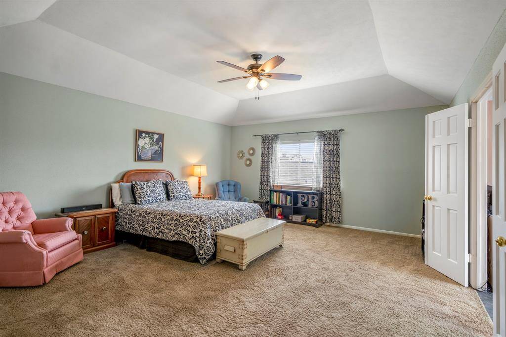 This is a spacious primary bedroom featuring vaulted ceilings, ceiling fan for added comfort, and plenty room for a sitting area.