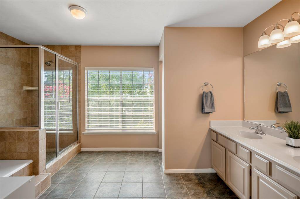 The spacious primary en-suite features a large walk-in shower with glass doors, a double vanity with plenty of storage, and a window offering natural light.