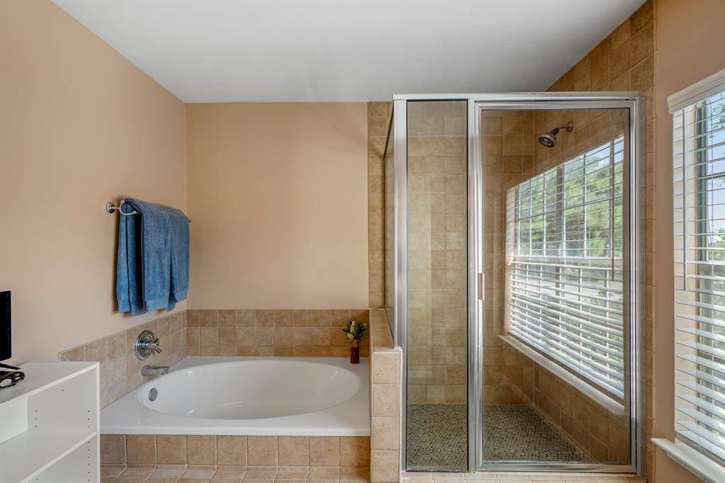 The primary bathroom features an over-sized corner bathtub, a separate glass-enclosed shower, and a window with blinds allowing for natural light.