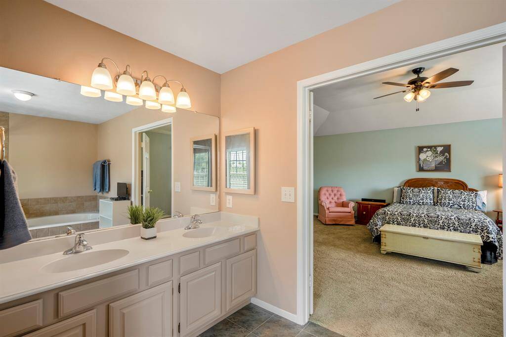 The en-suite master bathroom features dual vanities, a large mirror, and double doors leading directly into a spacious primary bedroom