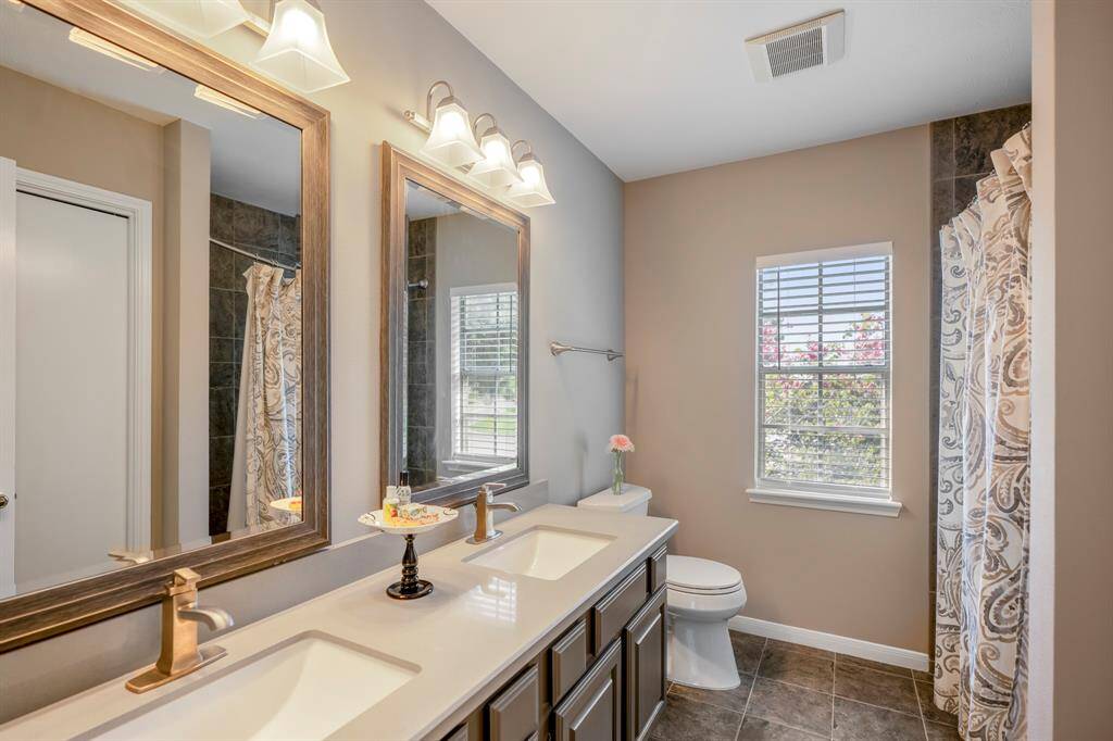 This remodeled secondary bathroom features a double vanity with silver fixtures, two large mirrors, and tiled flooring.