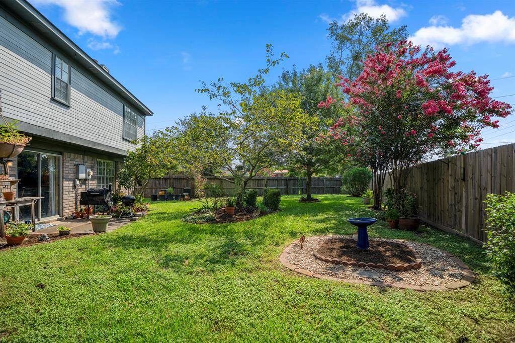 This backyard features mature flowering trees, complemented by a wooden privacy fence and a patio area for outdoor living.