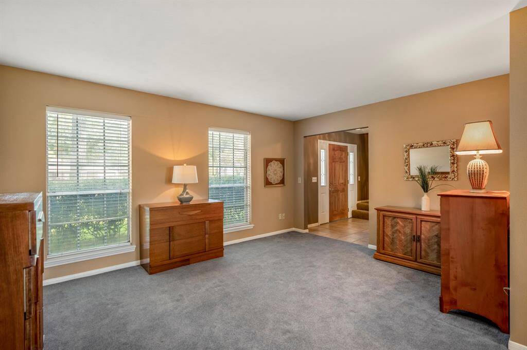 The formal living room features a warm neutral color palette, two large windows with blinds offering natural light.