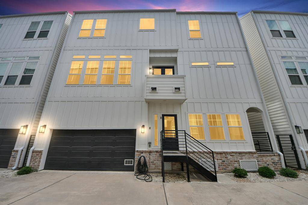 Modern three-story townhouse with a stylish facade featuring large windows and a welcoming entrance. It includes a two-car garage and a small balcony, perfect for a contemporary lifestyle.