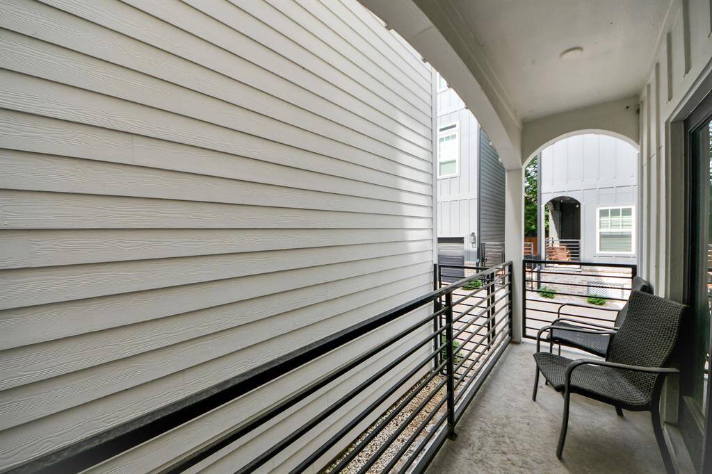 Cozy balcony with seating, enclosed by modern railing, offering a view of neighboring homes and a small courtyard area.