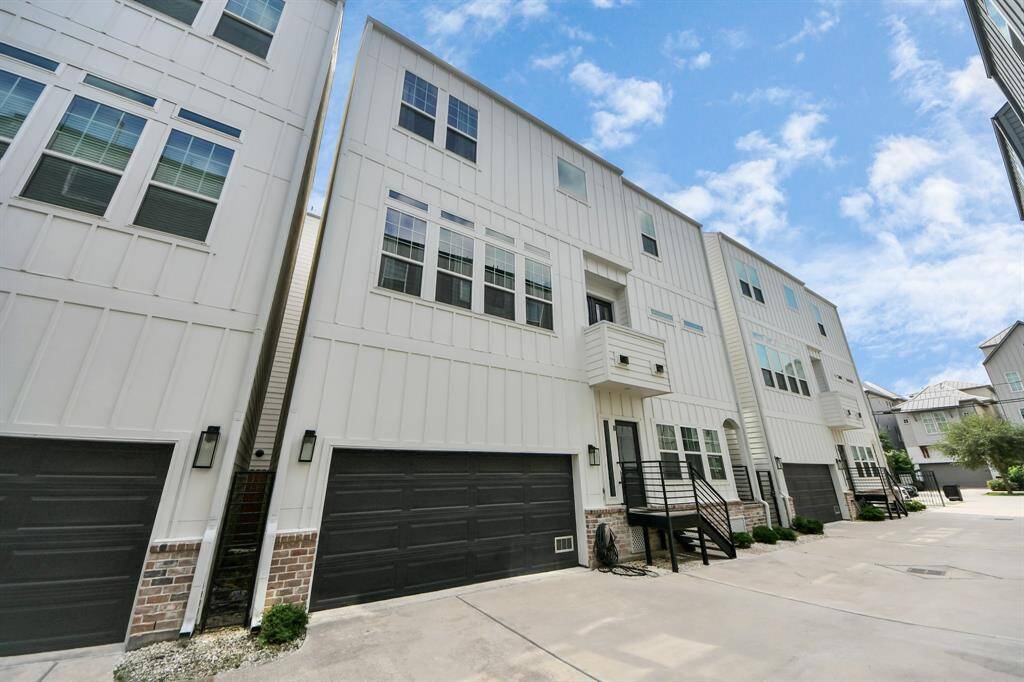 Modern townhouse with a clean, white exterior and black garage doors. Features multiple large windows for natural light and a small balcony. Situated in a neat, well-maintained neighborhood.