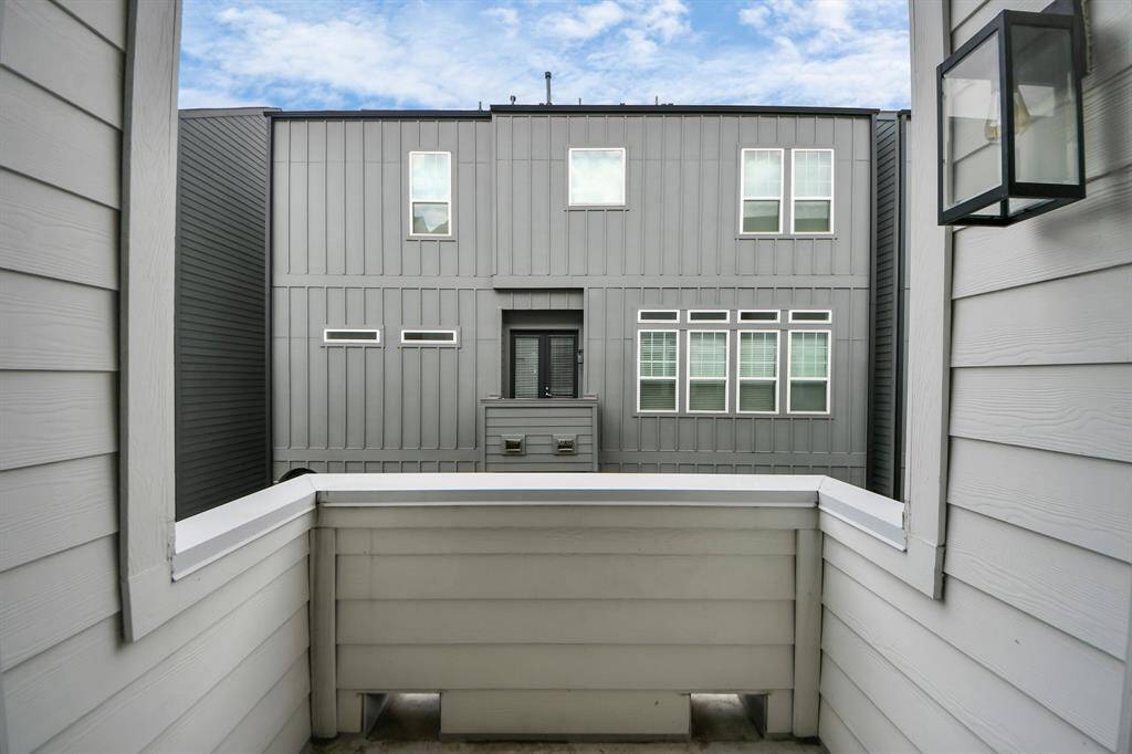 Compact balcony space with modern gray siding, providing a view of a neighboring building with large windows. Ideal for a small outdoor seating area.