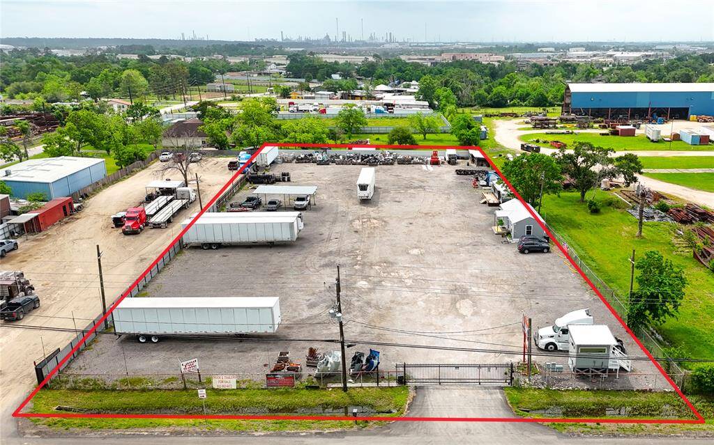 This photo shows a large, fenced commercial lot with ample parking and storage space. It features multiple trailers and vehicles, situated in an industrial area with greenery and industrial buildings in the background.