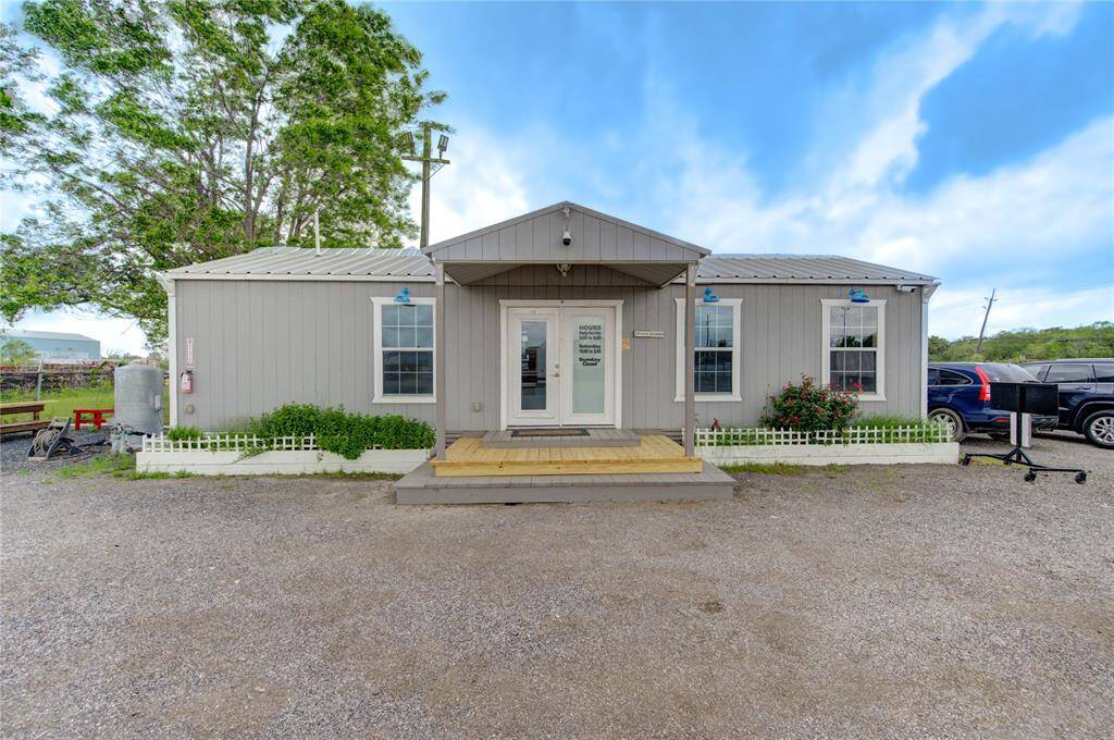 Charming single-story home with a rustic exterior, featuring a metal roof and quaint front porch. Surrounded by gravel and a small fenced garden, it offers a peaceful, rural vibe with ample parking space.