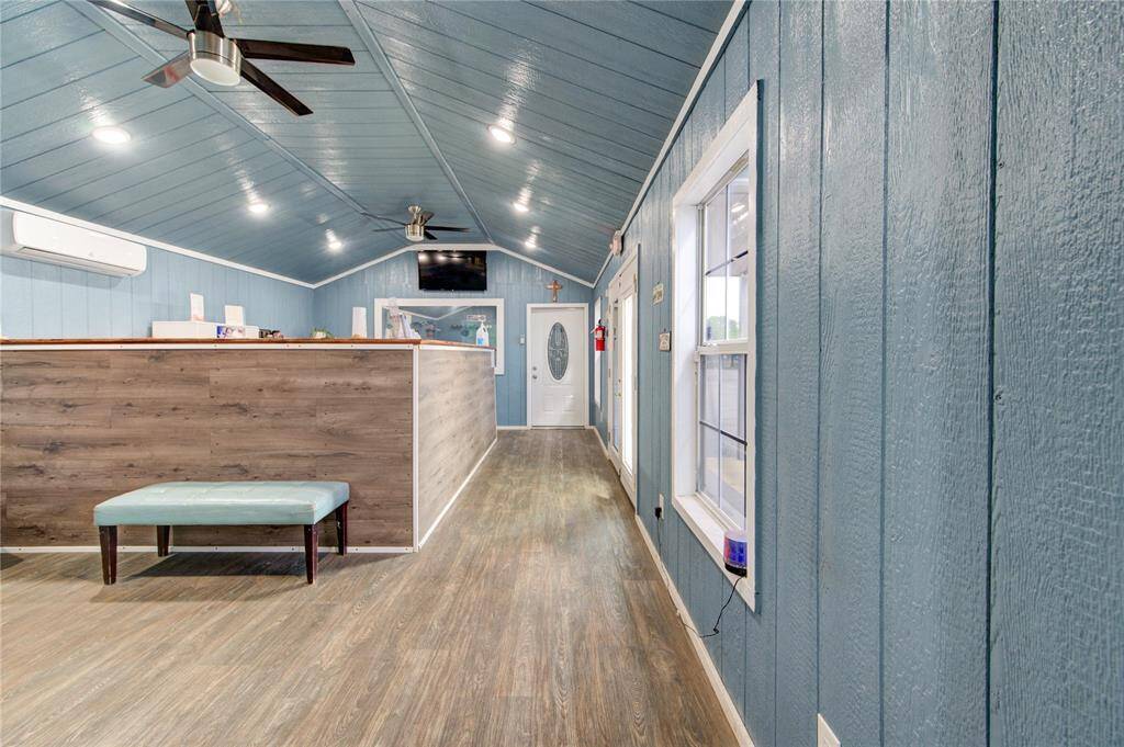This photo features a bright, spacious room with a vaulted ceiling and modern fans. The walls are painted a calming blue, complemented by wood-style flooring. Large windows provide natural light, and a sleek partition adds a touch of modern design.