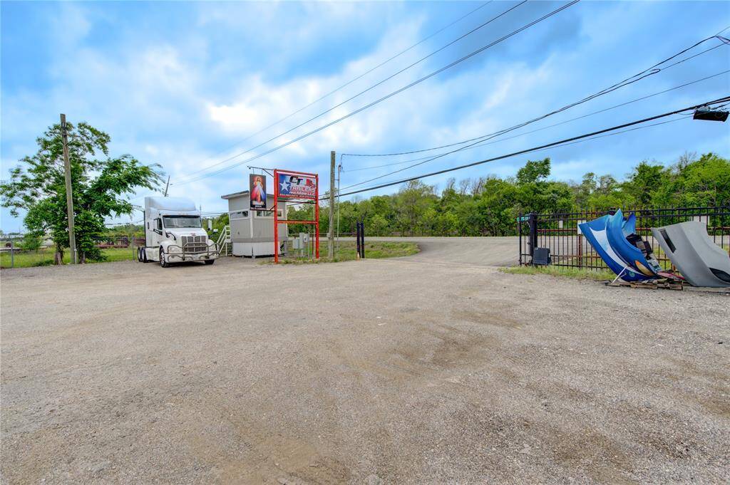 This photo shows a gravel lot with a semi-truck, surrounded by greenery. There's a small building with signage, and some industrial equipment nearby. Ideal for commercial use or storage.